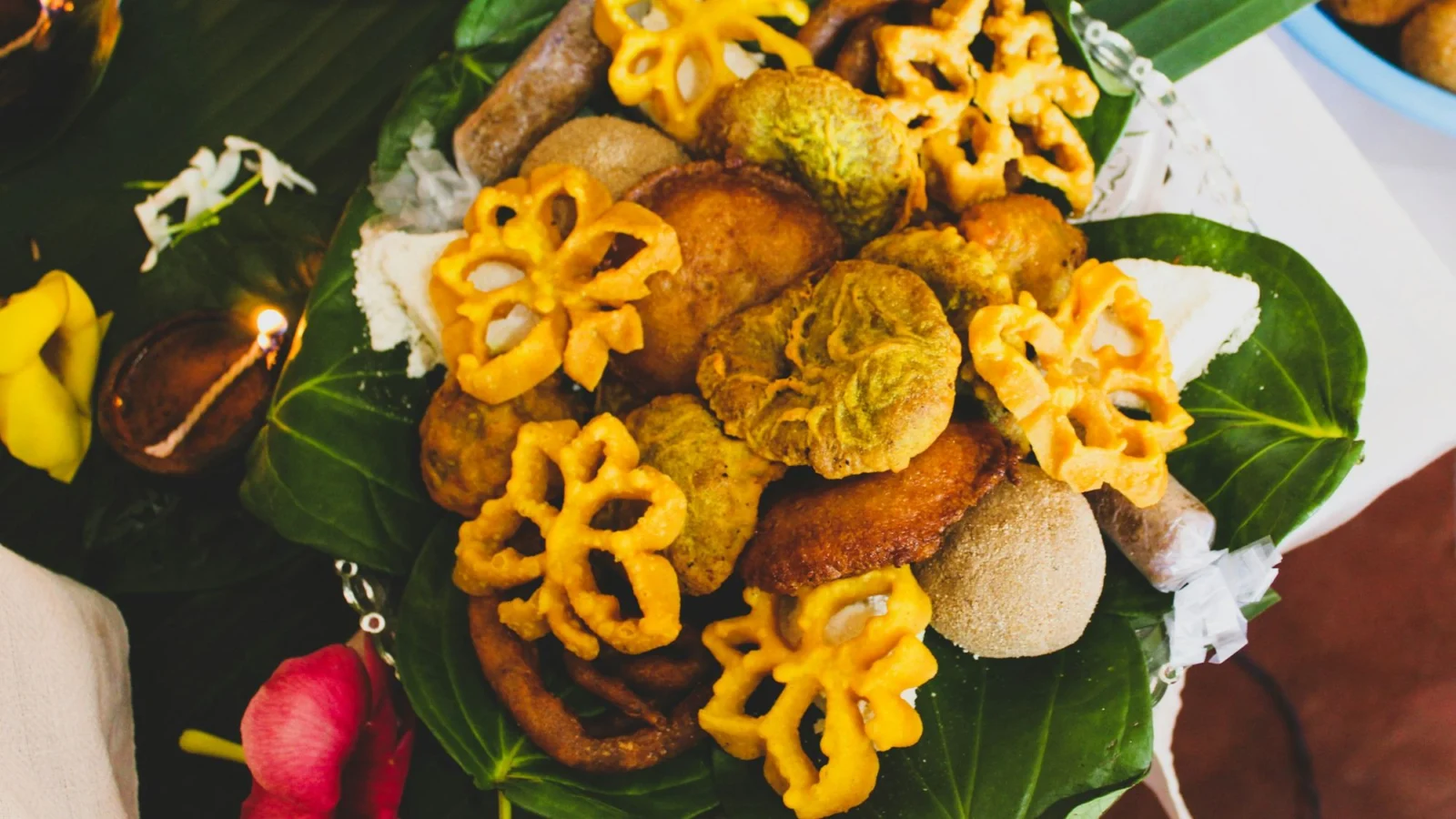 A tray of New Year sweets such as kokis, kavum and aluwa on betel leaves beside clay oil lamps