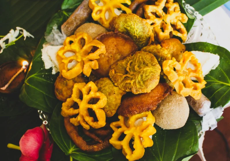 A tray of New Year sweets such as kokis, kavum and aluwa on betel leaves beside clay oil lamps