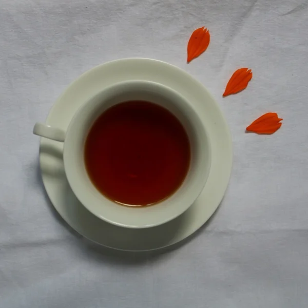 A white cup of bright red-amber black tea on a saucer, seen from above