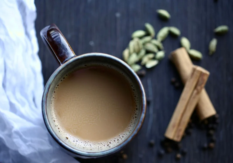 A mug of milk tea with green cardamom pods and cinnamon on dark wood