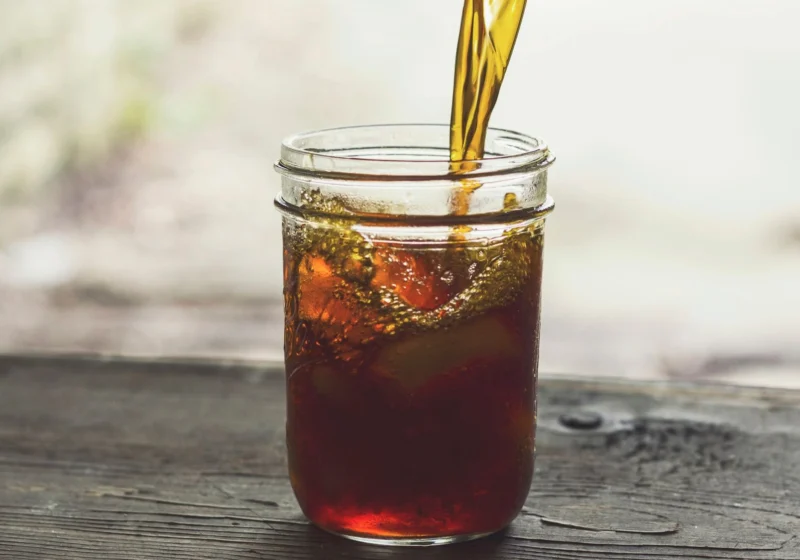 Amber tea poured over ice into a glass jar on weathered wood