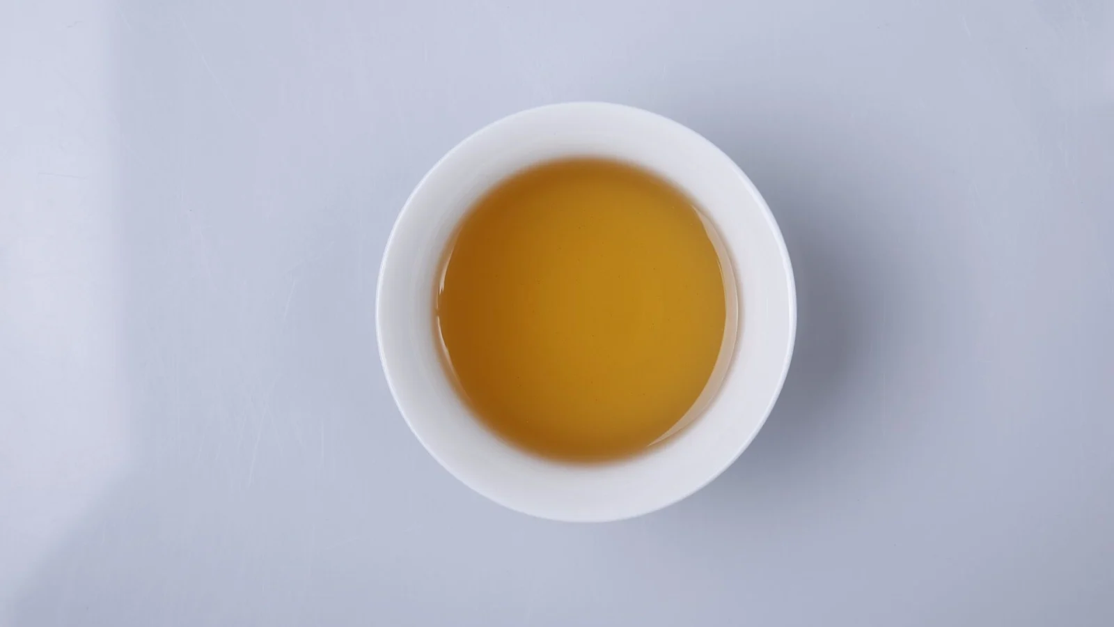 A white cup of bright golden-orange tea seen from above
