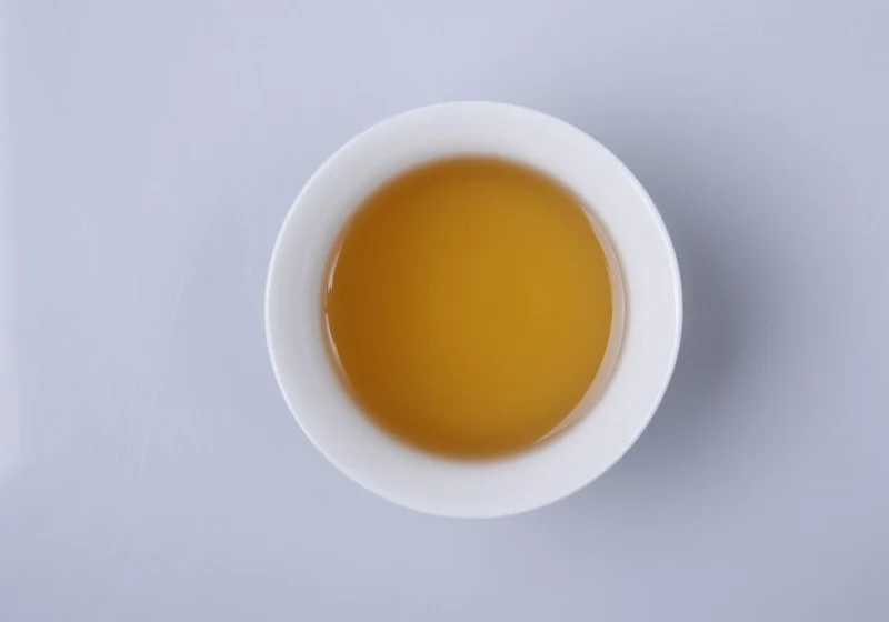 A white cup of bright golden-orange tea seen from above