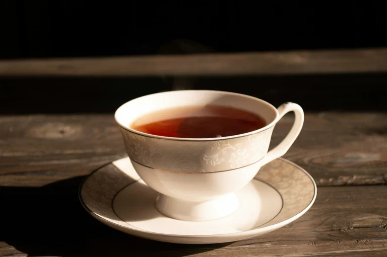 A white porcelain cup of red-amber black tea on a saucer in warm low sunlight