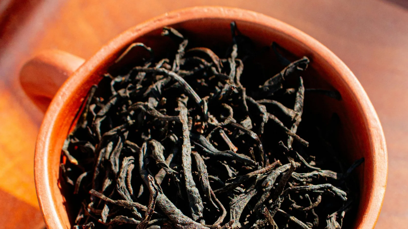 A terracotta cup filled with long, wiry dry black tea leaves