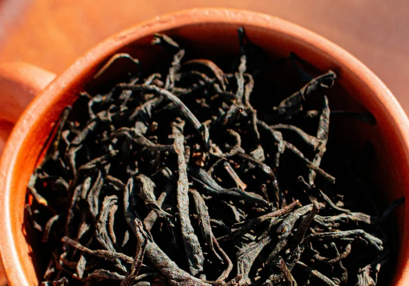 A terracotta cup filled with long, wiry dry black tea leaves