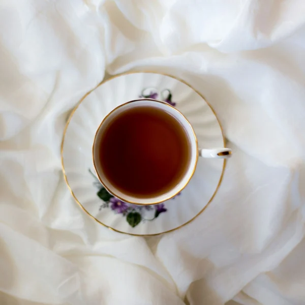 A gold-rimmed porcelain cup of deep red-brown black tea on white linen