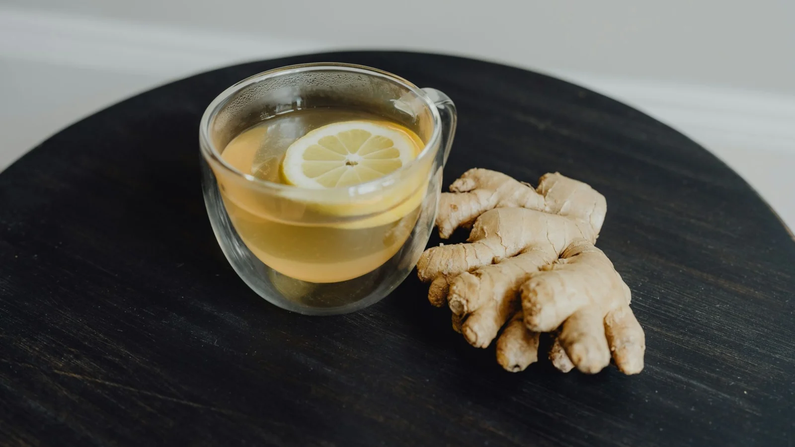 A glass cup of ginger tea beside a piece of fresh ginger root