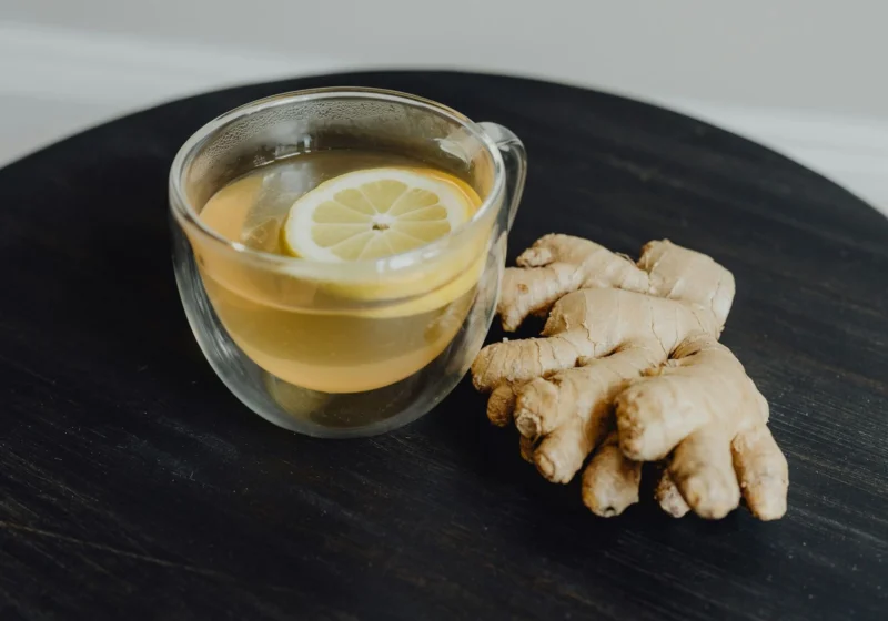 A glass cup of ginger tea beside a piece of fresh ginger root