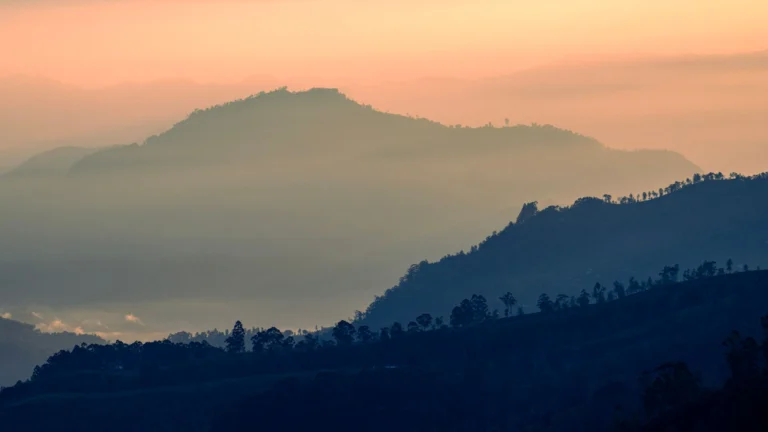 Layered hills silhouetted against a peach evening sky near Kandy
