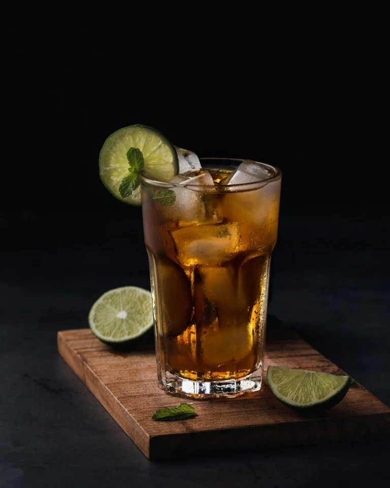 A glass of iced black tea with lime and mint on a wooden board