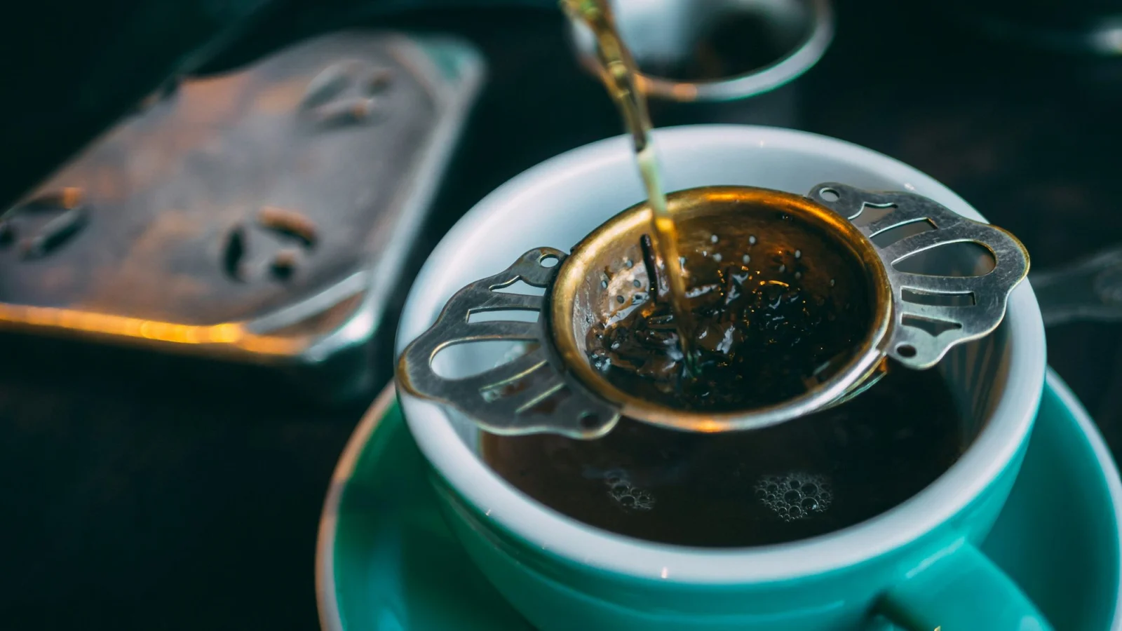 Black tea poured through a strainer of loose leaves into a cup