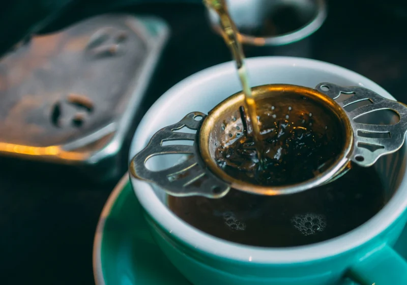 Black tea poured through a strainer of loose leaves into a cup