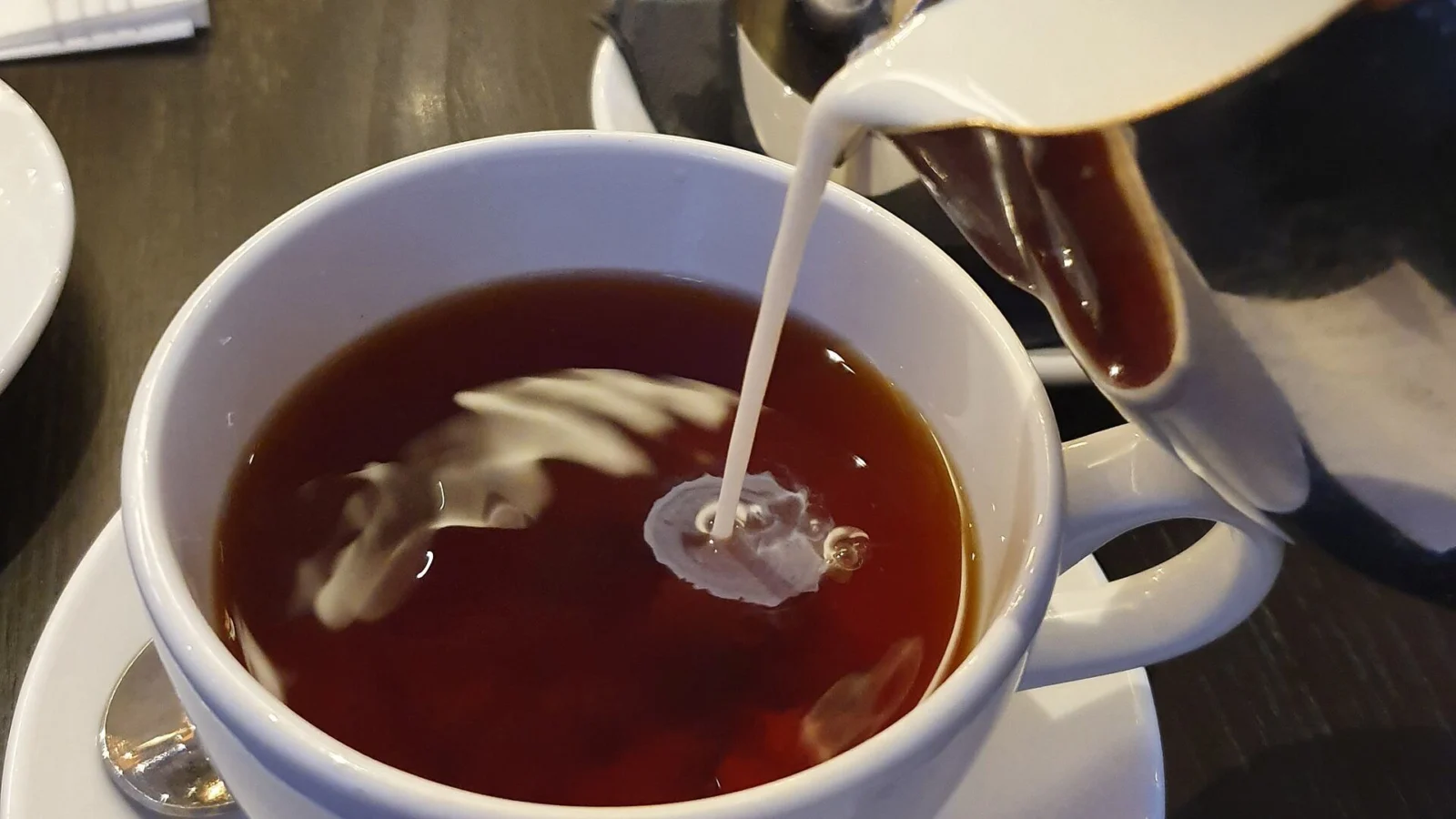 Milk streaming from a jug into a cup of dark black tea