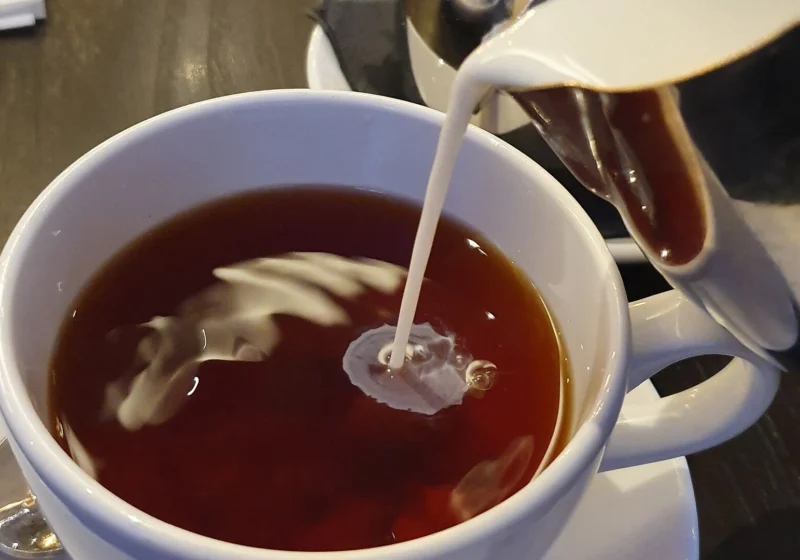 Milk streaming from a jug into a cup of dark black tea