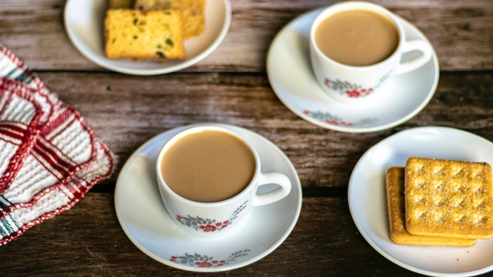 Two cups of milky tea with biscuits and cake on a wooden table
