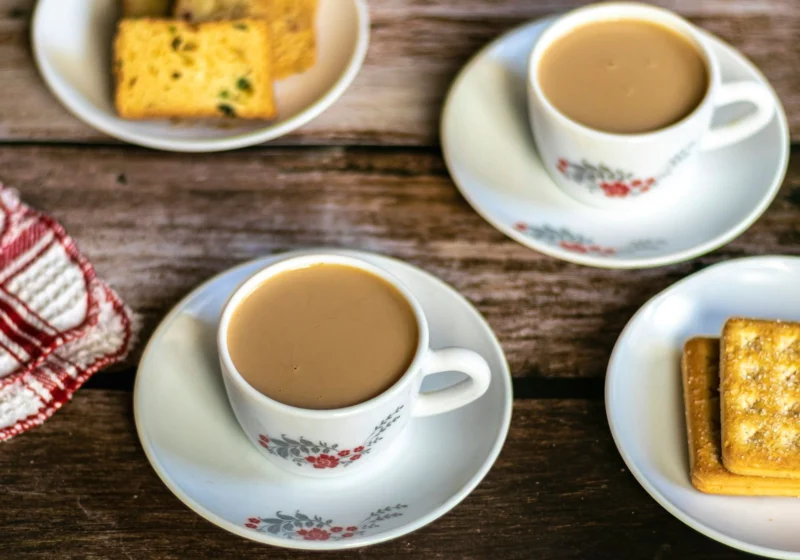 Two cups of milky tea with biscuits and cake on a wooden table