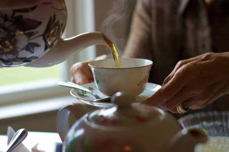 Tea being poured from a floral china teapot into a cup