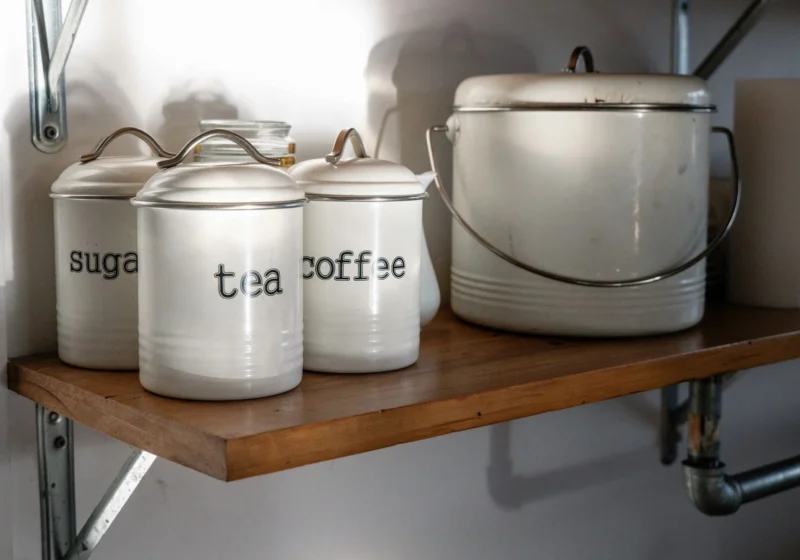 Lidded kitchen canisters, one marked tea, on a wooden shelf
