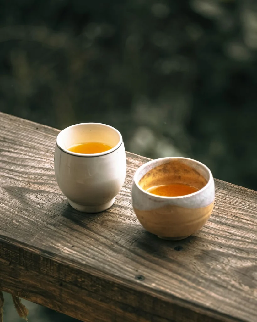 Two cups of amber Ceylon black tea on a wooden rail in warm morning light