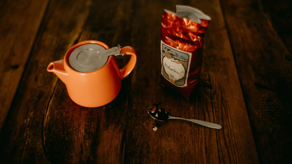 An orange teapot of loose tea beside a boxed tea bag on a wooden table